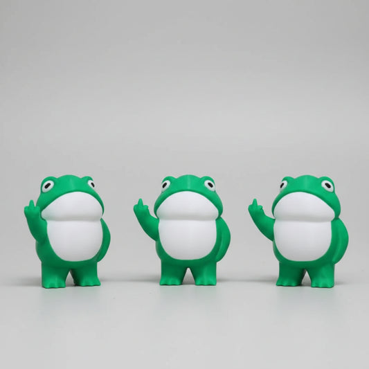 Three green frog figurines with white bellies on a concrete surface.
