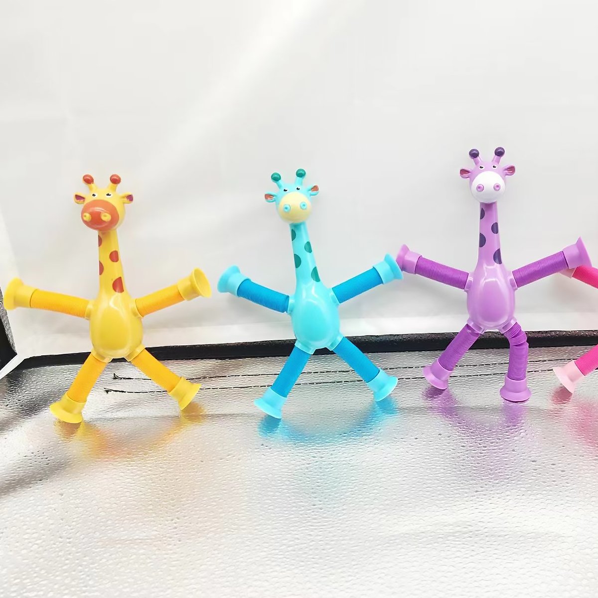 Three colorful giraffe-shaped toys on a reflective surface with a white background